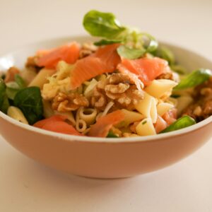 Delicious pasta salad featuring smoked salmon, walnuts, and fresh greens in a ceramic bowl.