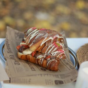 A mouthwatering croissant topped with chocolate drizzles and filled with fresh fruits, perfect for a cozy outdoor brunch.