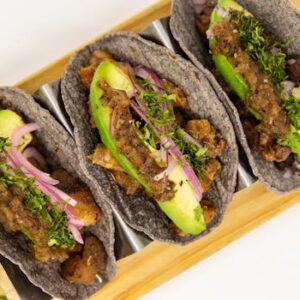 Close-up of blue corn tacos with avocado and vegetables on a metal tray.