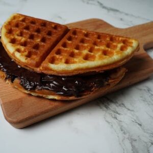 A close-up view of a waffle sandwich with rich chocolate spread on a wooden cutting board.