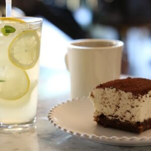 Close-up of a refreshing lemonade with a dessert and cup of coffee on a marble table, perfect for food enthusiasts.