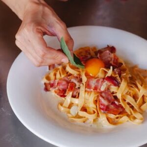 Delicious carbonara pasta with bacon and egg yolk garnished with fresh basil. Perfect for food lovers.